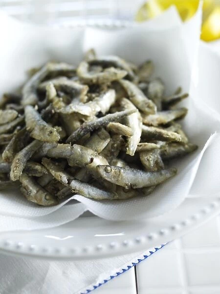Fried whitebait on kitchen paper in bowl, close-up