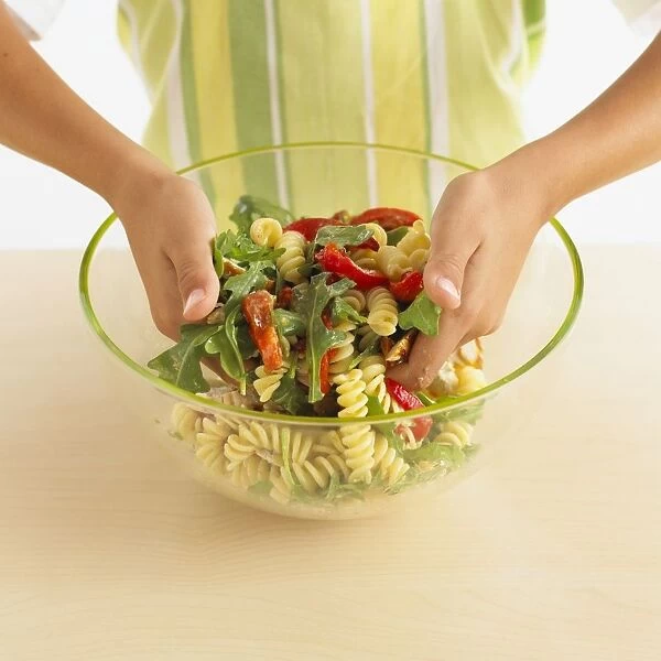Girl mixing pasta salad with her hands, close-up