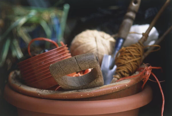 Large terracota pot containing stacked plastic pots, spade, trowel and spools of string, close up