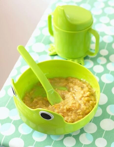 Lentil and carrot puree in green bowl with spoon embedded, and green mug with spout