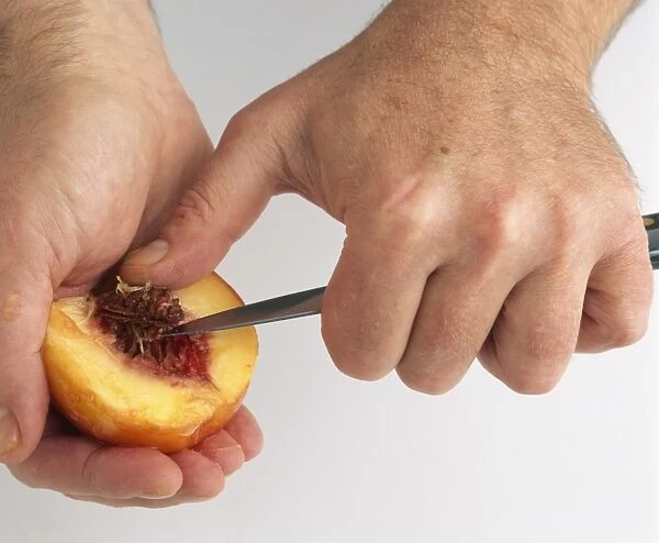 Mans hand removing peach stone with knife, close-up