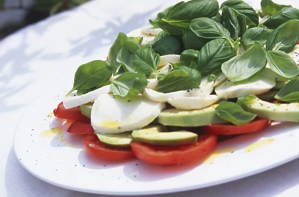 Mozzarella, tomato and avocado salad garnished with whole basil leaves and served on white plate