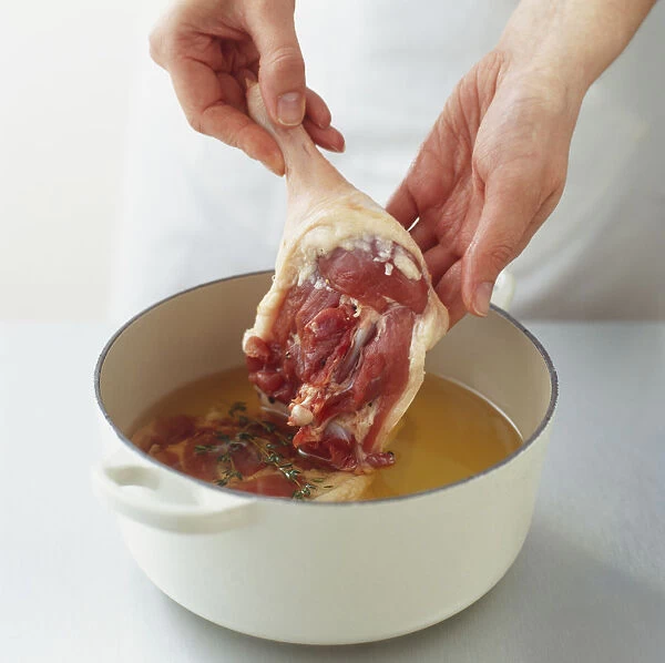 Placing pieces of raw duck in a pot of liquid fat