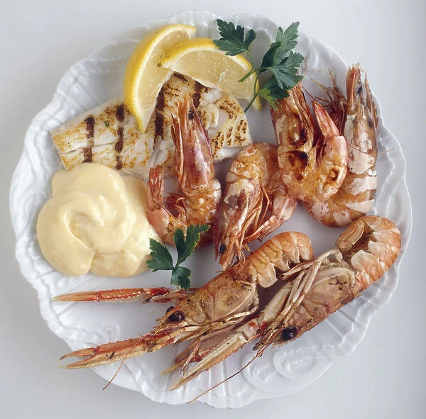Plate of grilled fish and prawns served with mayonnaise, lemon slices and parsley, view from above