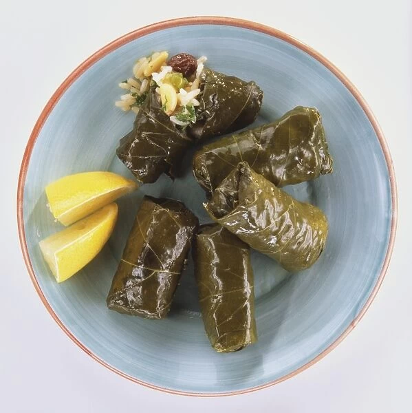 Plate of five stuffed vine leaves, one split open to show rice stuffing, garnished with lemon wedges, overhead view