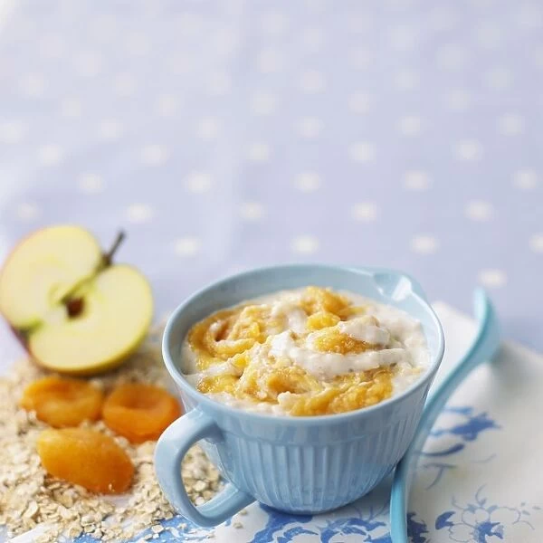 Porridge with apples and and apricots in blue cup, with ingredients and a spoon nearby, close-up