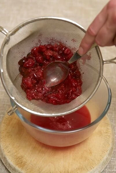 Pressing cranberries through a sieve with a spoon to produce smooth pulp in the bowl