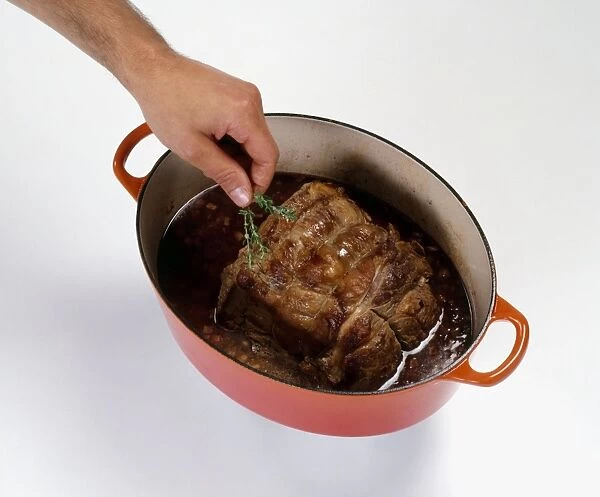 Putting sprig of thyme in casserole dish containing silverside of beef and red wine sauce