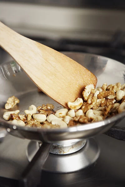 Roasting cashew nuts and walnuts on gas hob using wooden spatula to stir