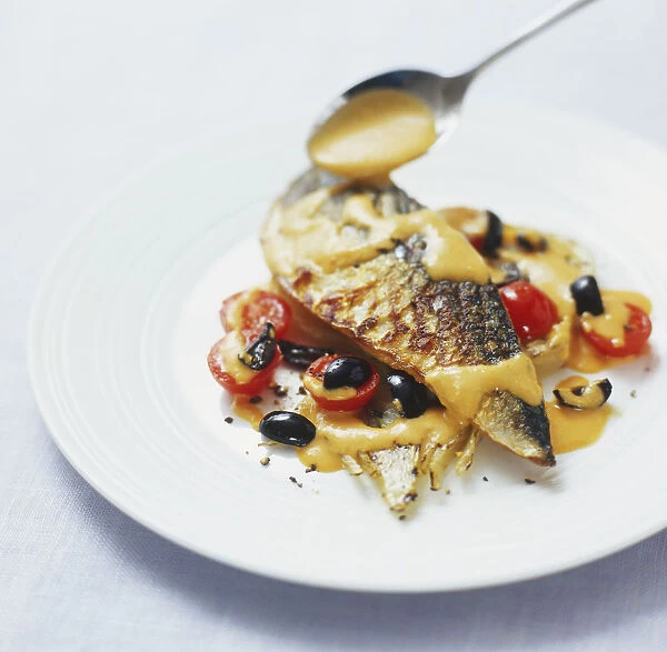 Romesco sauce being spooned over grilled mackerel fillet served with black olives and cherry tomatoes