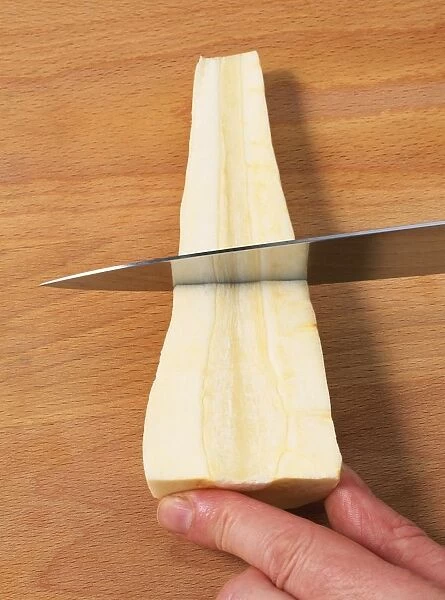 Using kitchen knife to slice parsnip on chopping board