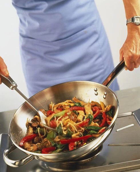Using metal kitchen utensils to stir-fry strips of pork in wok with red and green peppers, mushrooms and spring beans, blurred motion