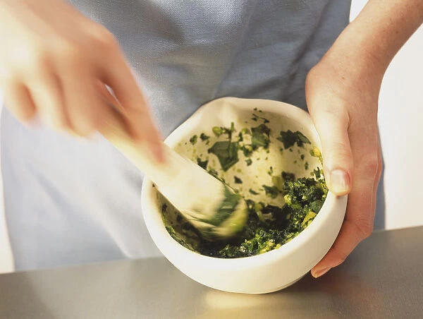 Using pestle to pound basil leaves and garlic in mortar, blurred motion
