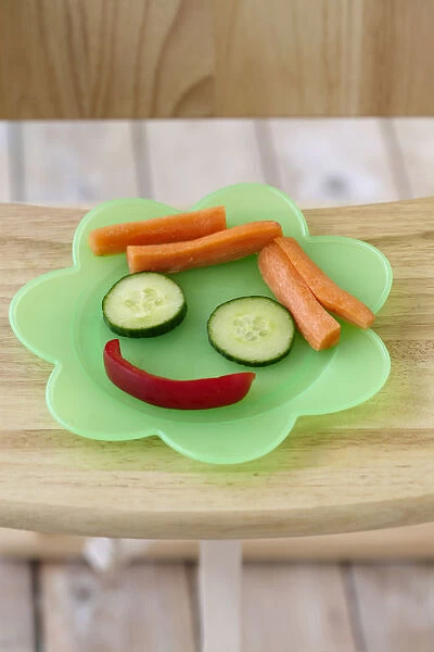 Vegetables arranged to form a face, on a plastic plate