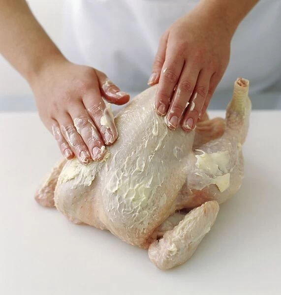 Womans hands rubbing butter onto raw chicken, close-up