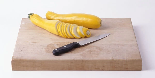Yellow courgettes, whole and sliced, on wooden chopping board with kitchen knife