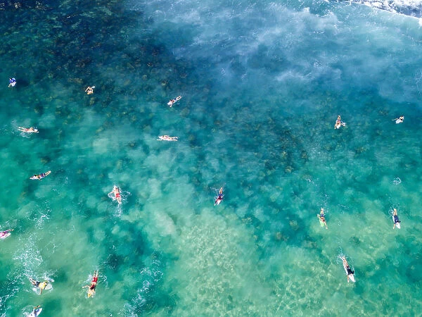 Aerial View over blue and green clear ocean waters with surfers