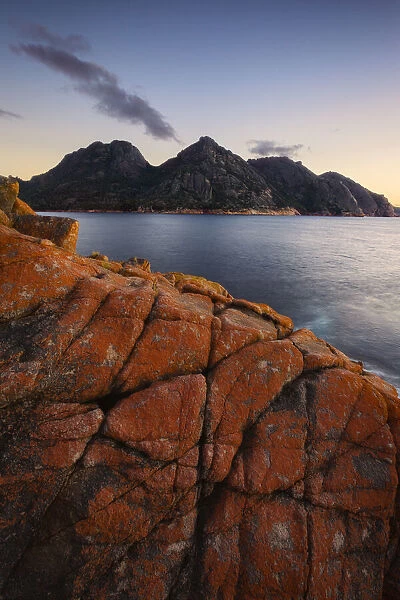 Dawn over Wineglas Bay and a section of rock covered in red lichen with the Hazards