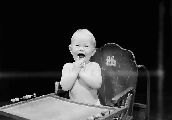 Baby boy (6-11 months) sitting in high chair and laughing