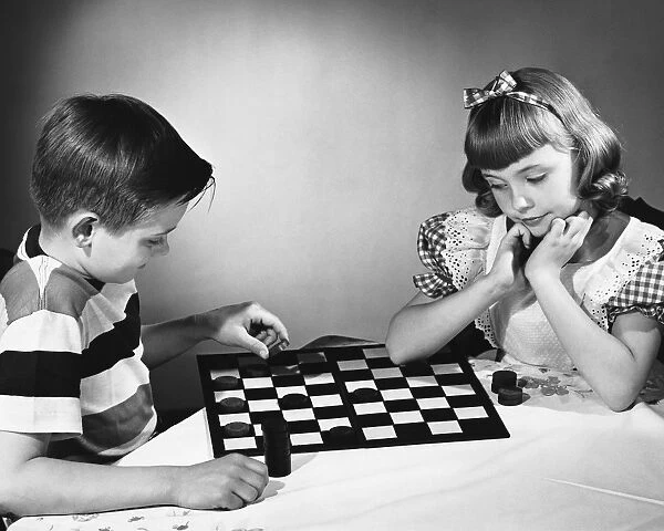 Brother and sister playing checkers at table