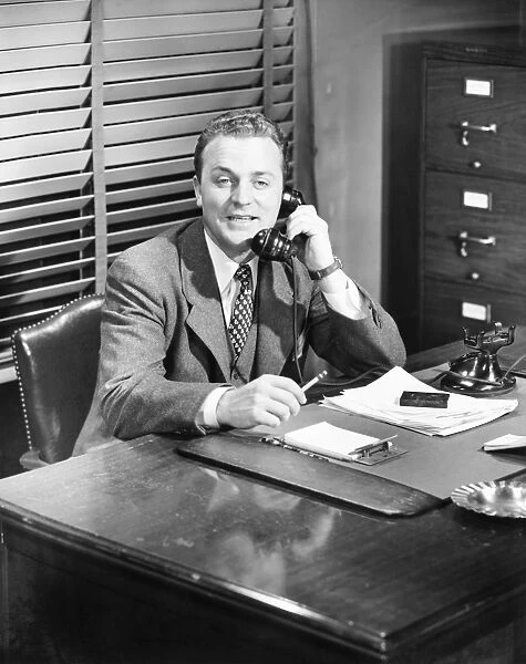 Businessman talking on phone at desk (B&W)