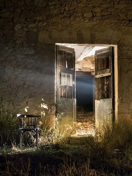 Door of a house in ruins opened in the night with a beam of light