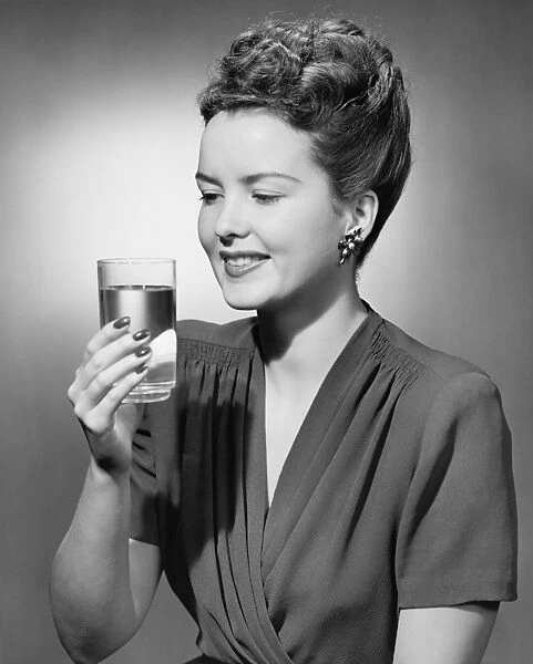 Elegant woman holding glass of water in studio, (B&W), portrait