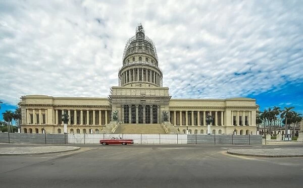 Havanas Capitol building with red vintage car and dramatic sky, Cuba