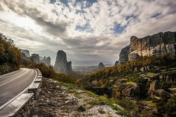 Landscape of rugged cliffs, road, autumn foliage and Monastery Rousanou in the distance