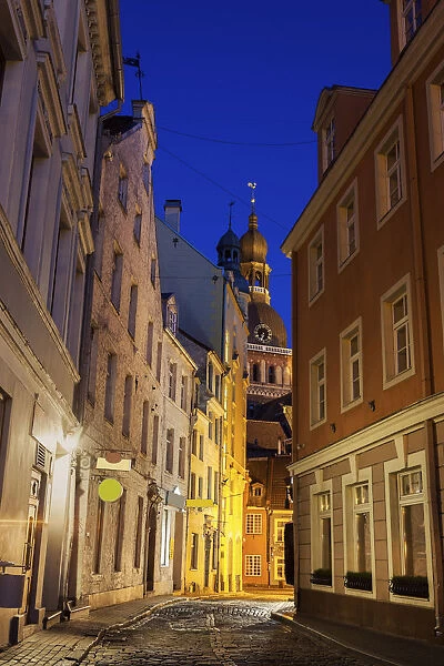 Latvia, Riga, View of illuminated street in old town and Riga Cathedral at dusk