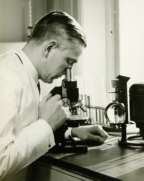 Male doctor using microscope in surgery, (B&W)