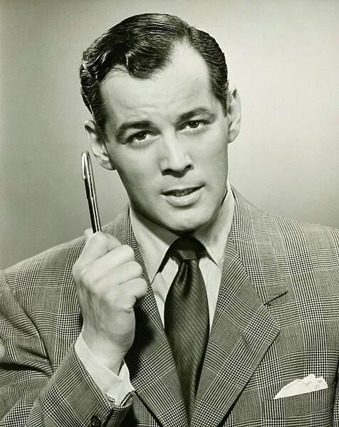 Man holding ballpoint, posing in studio, (B&W), portrait
