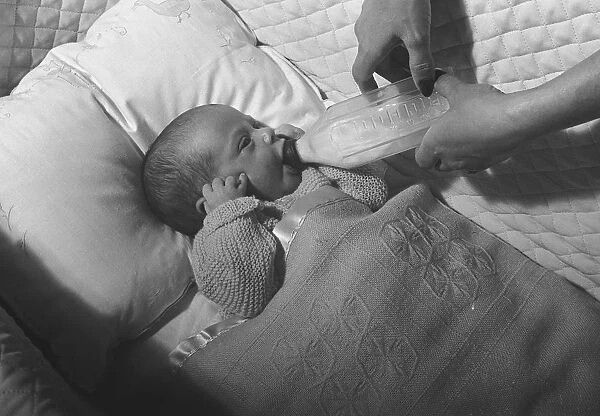 Mother feeding baby (0-3 months) lying in crib with baby bottle, (B&W), close-up