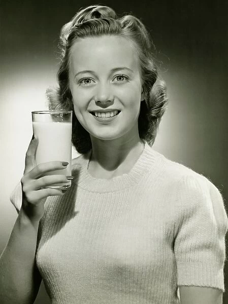 Smiling woman holding glass of milk in studio, (B&W), portrait