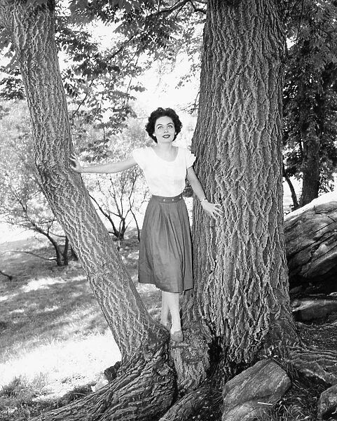 Woman posing between two tree trunks, (B&W), portrait