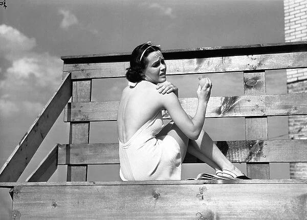 Woman sunbathing, applying sun cream on shoulder, (B&W)
