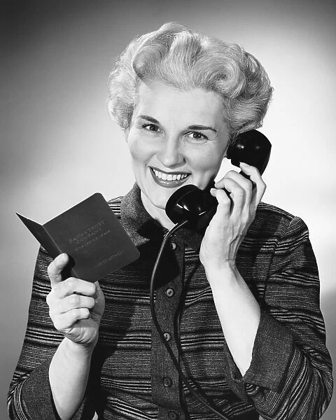 Woman using phone, holding small book in one hand