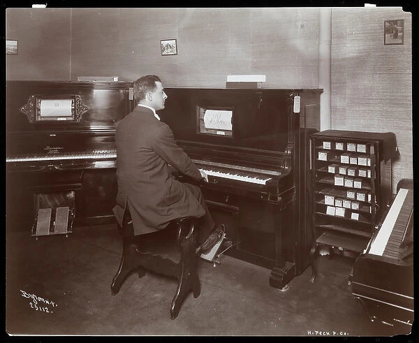 A man playing a player piano in a piano showroom in New York, 1907 (silver gelatin print)