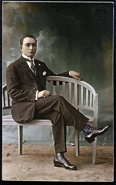 Portrait of elegant young man looking like dandy posing sitting on a bench. He wears varnished shoes, a ring and adopted an affected attitude. 1920-1930