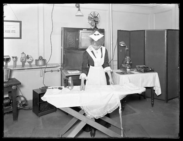 Young woman in a maids costume demonstrating the use of an electric iron, c