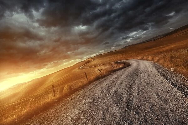 A country road in field at sunset against stormy clouds, Tuscany, Italy