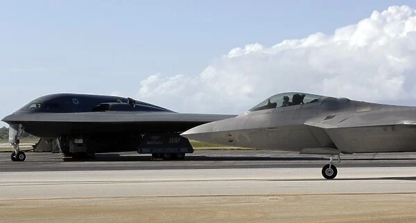 An F-22 Raptor taxis while a B-2 Spirit waits for clearance