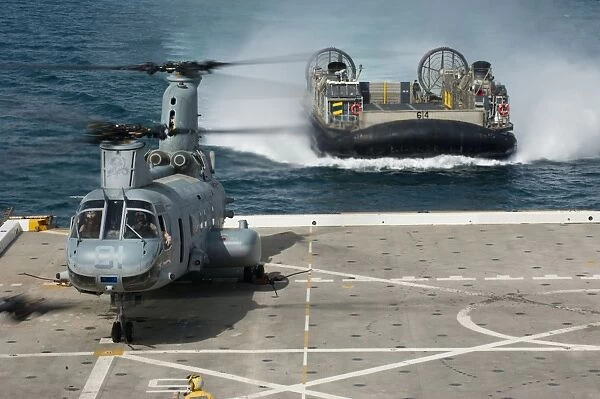 A hovercraft approaches USS New Orleans as a CH-46E Sea Knight sits on the flight deck