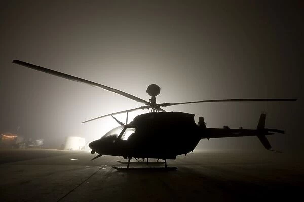 The illumination from the bright light silhouettes a OH-58D Kiowa helicopter during