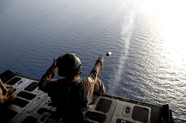 A loadmaster throws a smoke grenade out of an HC-130 aircraft