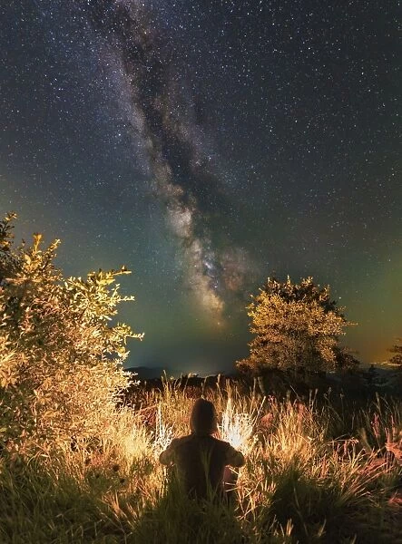 Man sitting near the campfire in the forest under the stars and Milky Way, Sudak, Crimea