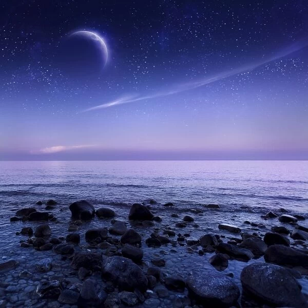Moon rising over rocky seaside against starry sky