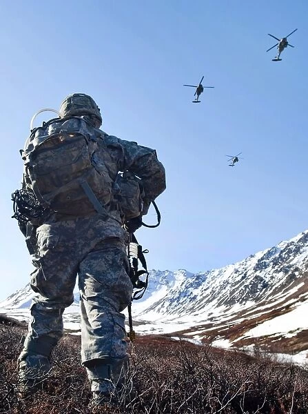 Soldier patrols through Alasks Chugach Range as UH-60 Black Hawk helicopters fly above