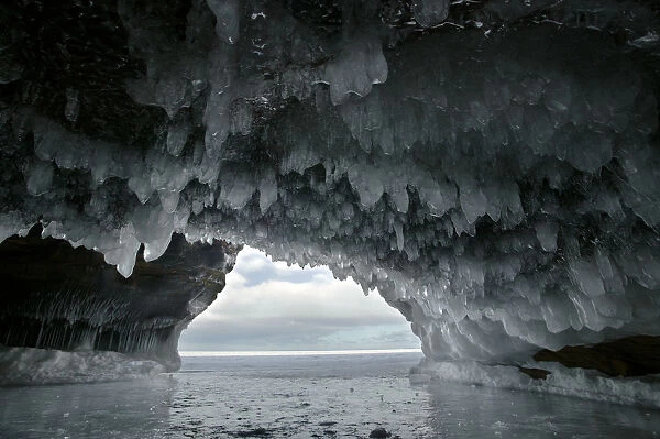 Ice hanging from arch in sea cave carved in soft sandstone cliffs, frozen lake, Squaw Bay