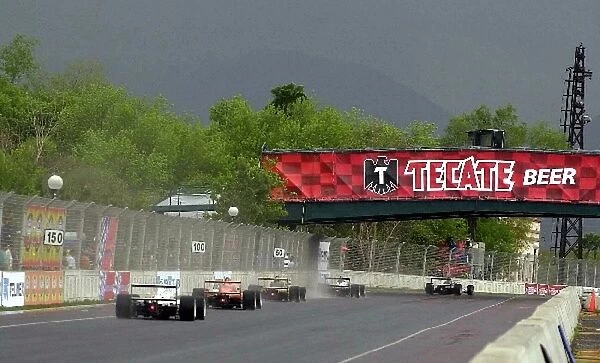 A gaggle of midfielders make their way under the Tecate bridge and into turn one